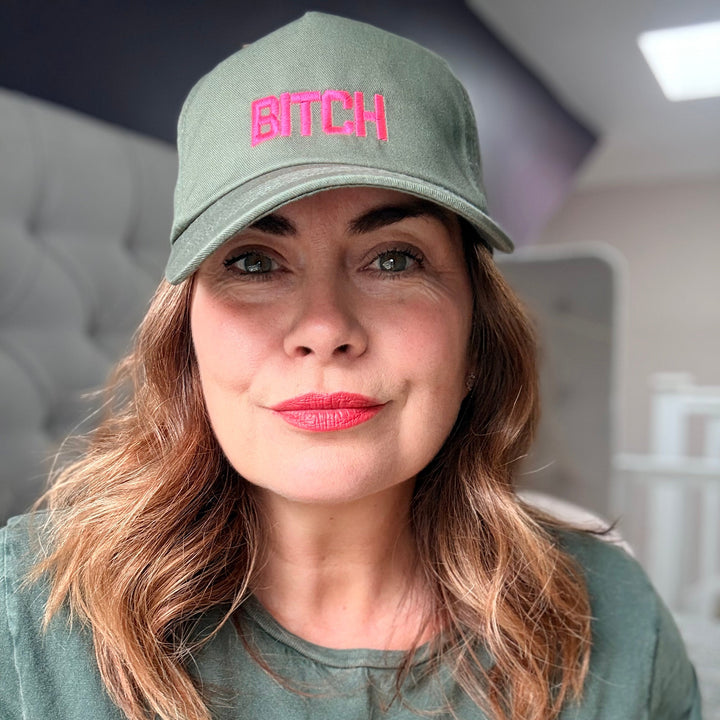 Person wearing a green cap with pink text and a green shirt with orange text, indoors.