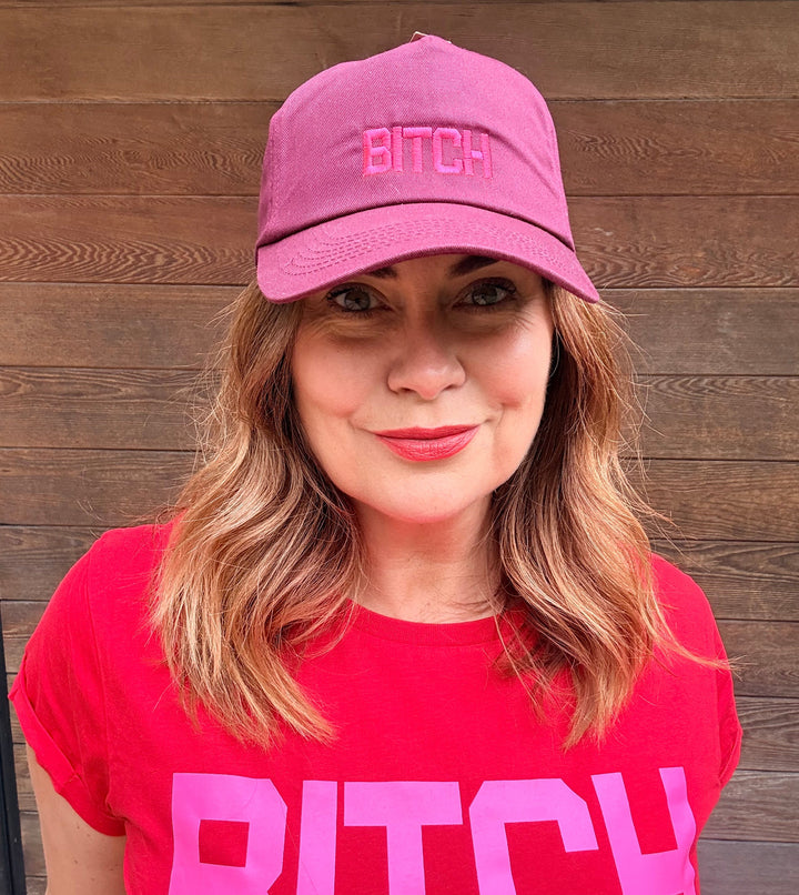 Person wearing a pink cap and shirt with bold text on a wooden floor background